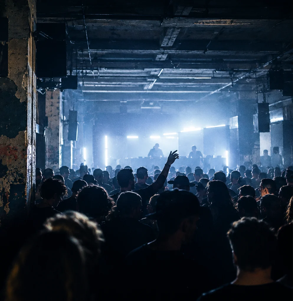 A dark warehouse floor packed with people facing the DJ booth