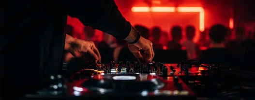 A DJ's hands working a mixer under red light